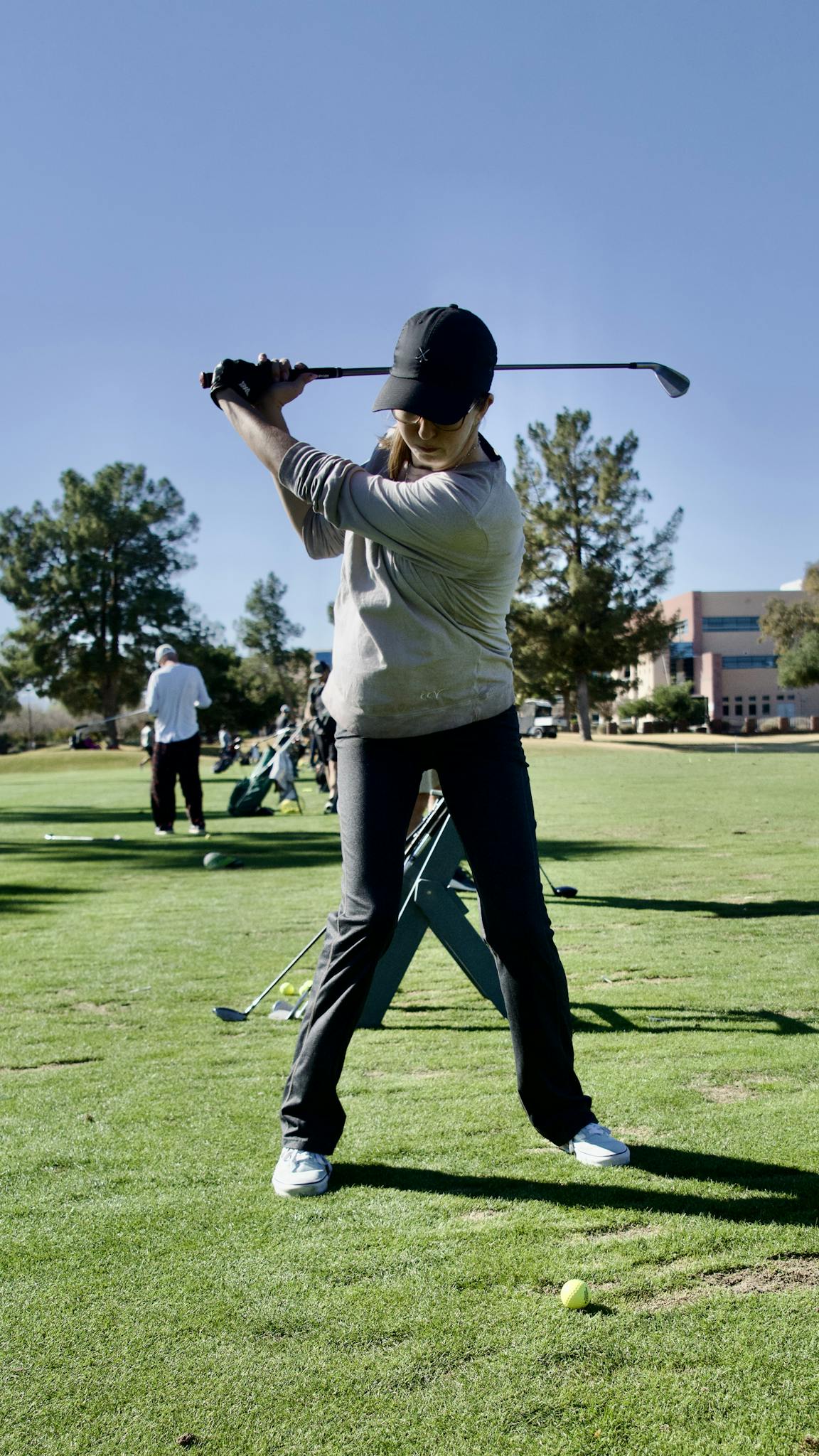 A woman golfer in mid-swing on a sunny golf course, practicing her technique.